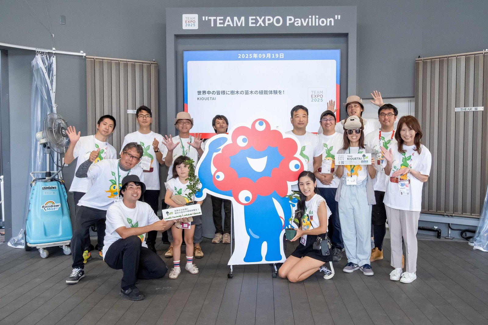 TEAM EXPOパビリオンで、苗木を囲むメンバーの集合写真